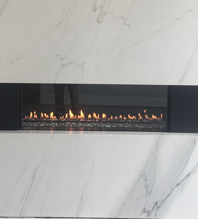 A slim linear fireplace framed by pale marble