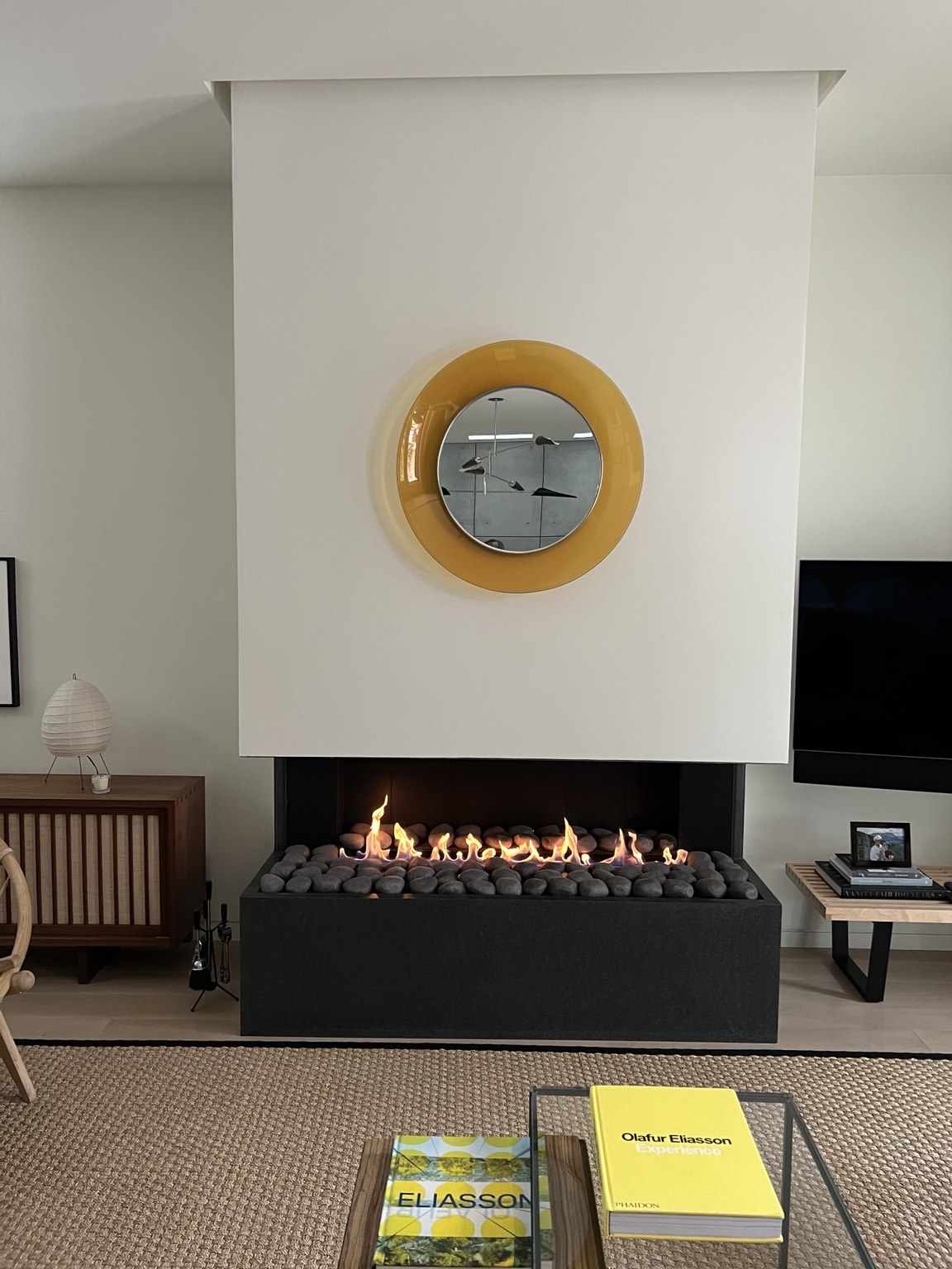 A welcoming living room with a glowing decorative fireplace and a yellow round mirror