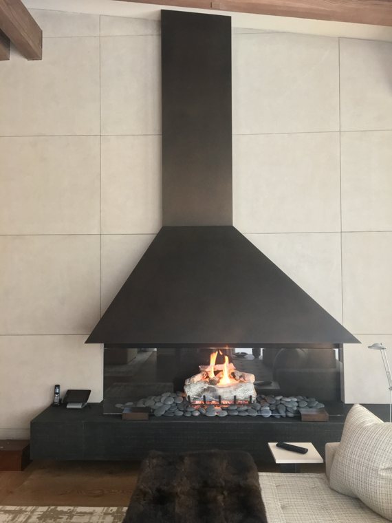 A fireplace with a tall black steel hood and stone media in a living room